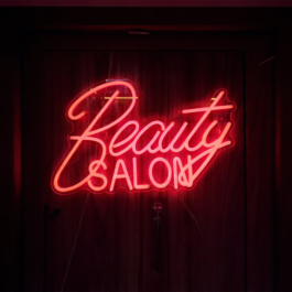 Vibrant red and pink "Beauty Salon" LED neon sign mounted on a dark wooden door.
